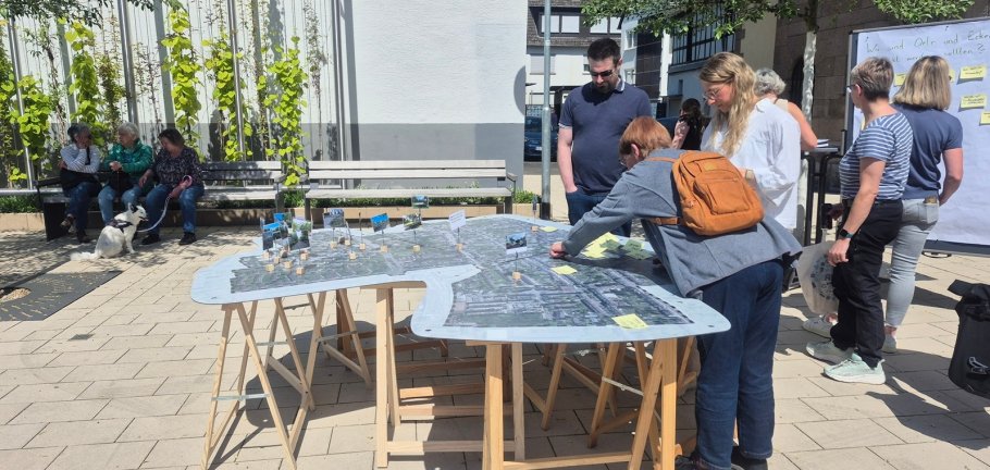 Menschen stehen an einem Tisch und betrachten eine abgebildete Landschaft.
