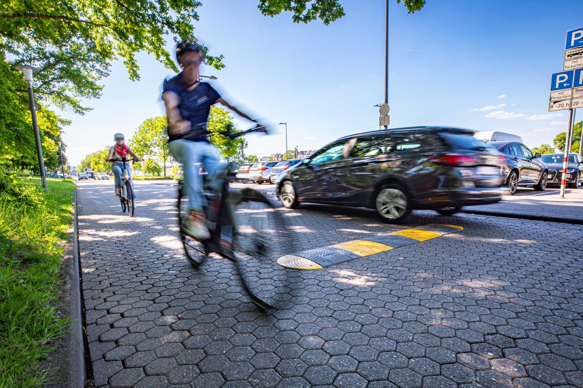 Zwei Fahrradfahrer und ein Auto fahren auf einer Straße.