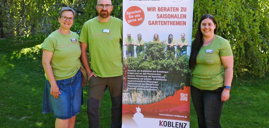 Zwei Frauen und ein Mann stehen vor einem Werbebanner.