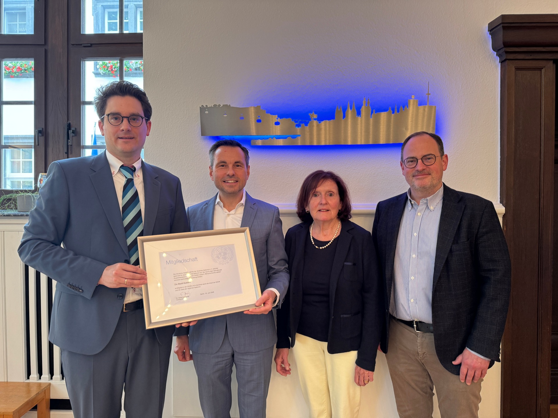 Gerrit Pursch (1.v.l., Vorsitzender des Landesverbandes Rheinland-Pfalz/Saarland der DGVN) und Ursula Mogg, (2.v.r., Mitglied des Bundesvorstandes der DGVN) überreichen Oberbürgermeister David Langner (2.v.l.) und Kultur und Bildungsdezernent Ingo Schneider (1.v.r.) die Mitgliedsurkunde der DGVN. 
