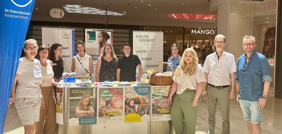 Frauen und Männer stehen an einem Infostand. Frauen und Männer stehen an einem Infostand.