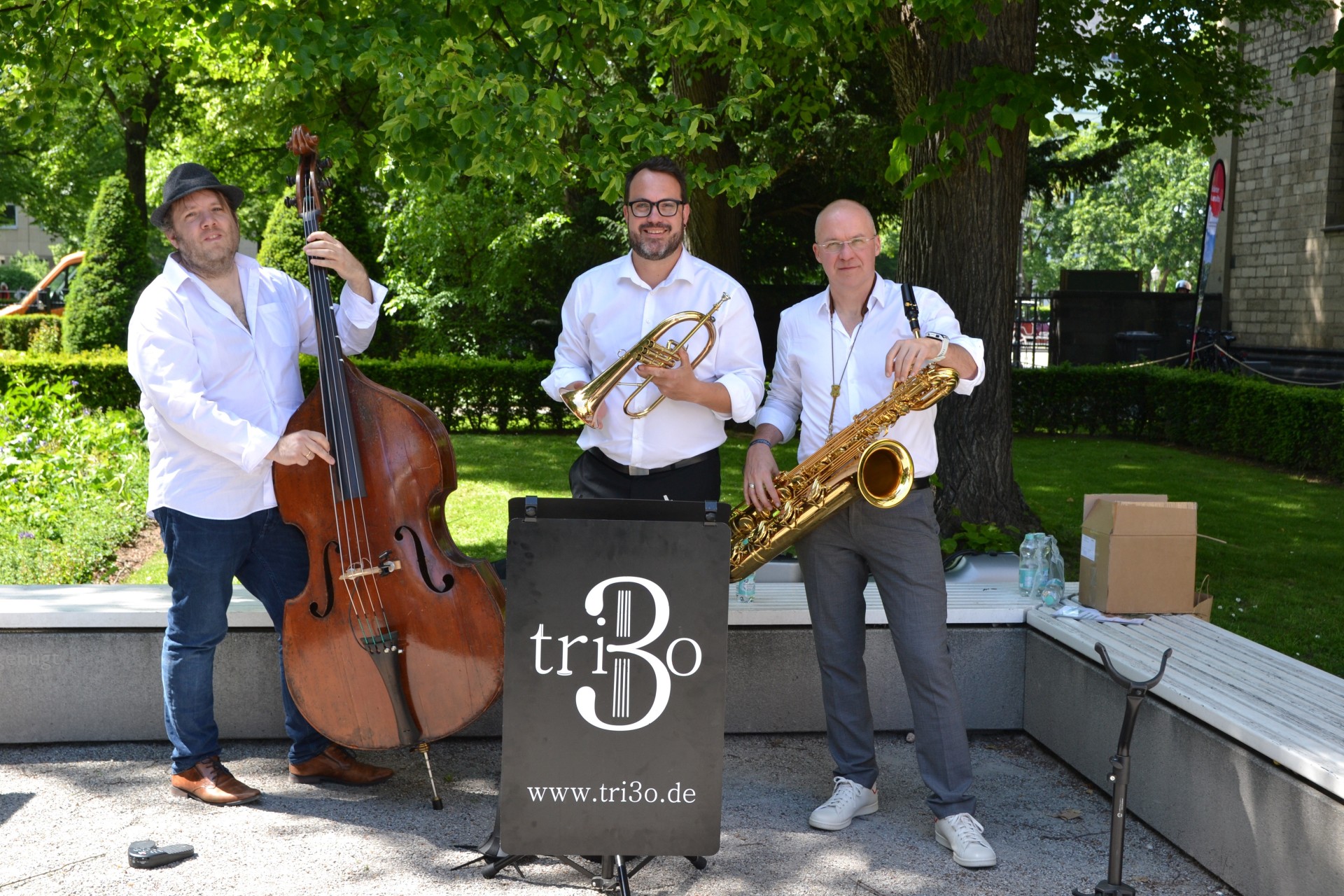 Drei Männer stehen mit Instrumenten in einem Park.