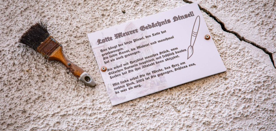 Ein Pinsel und eine Informationstafel hängen an einer Hauswand. Ein Pinsel und eine Informationstafel hängen an einer Hauswand.