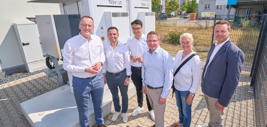 Sechs Personen stehen vor einem Batteriespeicher. Sechs Personen stehen vor einem Batteriespeicher.