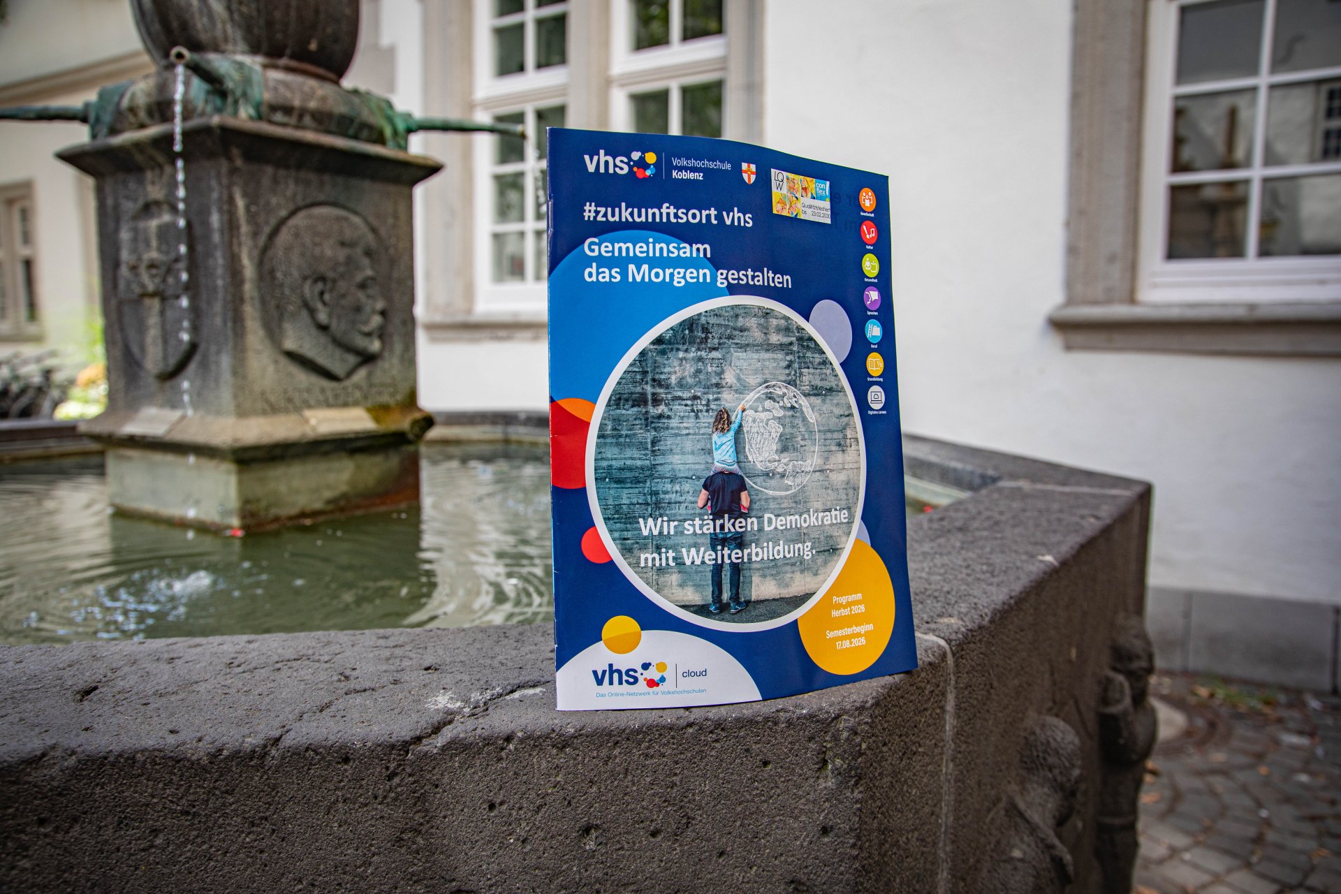 Das neue Programmheft der Volkshochschule Koblenz auf dem Schängelbrunnen