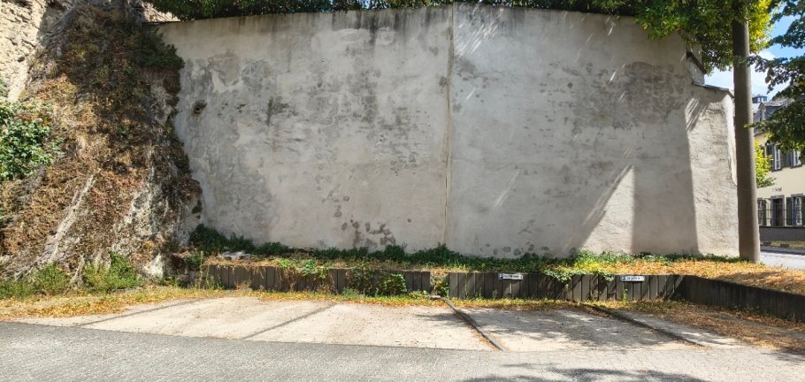Eine leere, weiße Wand grenzt an einen Parkplatz.