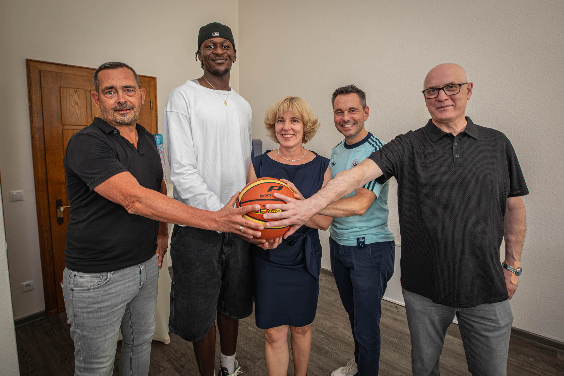 Fünf Personen fassen an einen Basketball und schauen in eine Kamera.
