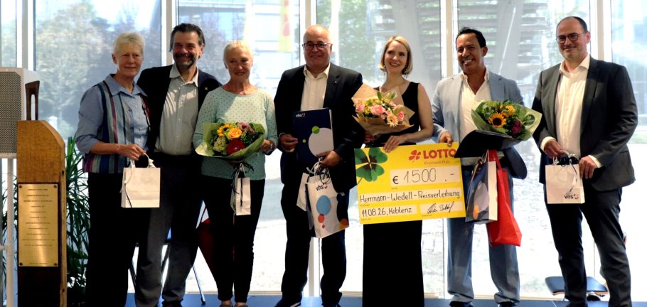 Drei Frauen und vier Männer stehen für ein Ehrungsfoto vor einer Kamera.