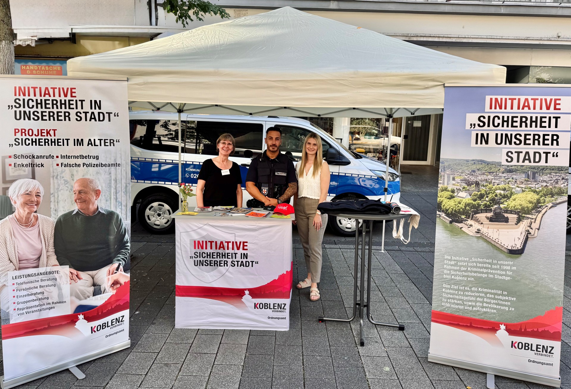 Zwei Frauen und ein Mann stehen an einem Informationsstand.