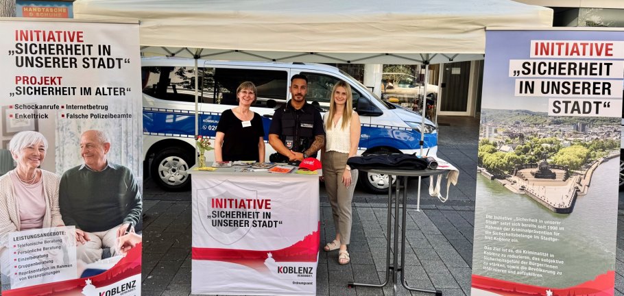 Zwei Frauen und ein Mann stehen an einem Informationsstand.