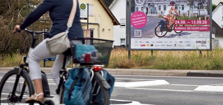 Eine Radfahrerin fährt an einer Plakatwand vorbei. Eine Radfahrerin fährt an einer Plakatwand vorbei.