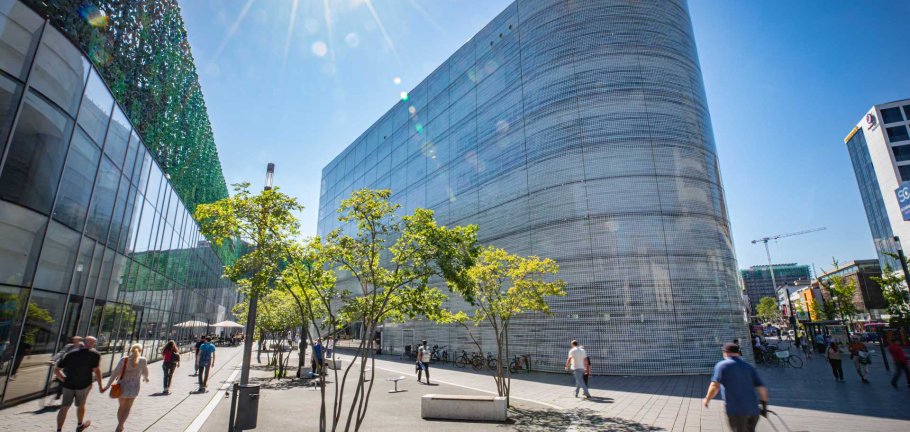 Ein Gebäude mit einer Glasfront steht auf einem belebten Platz. Ein Gebäude mit einer Glasfront steht auf einem belebten Platz.