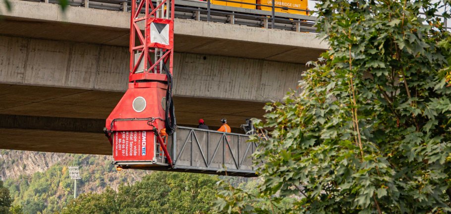Bauarbeiter kontrollieren von einem Unterflurgerät aus eine Brücke.