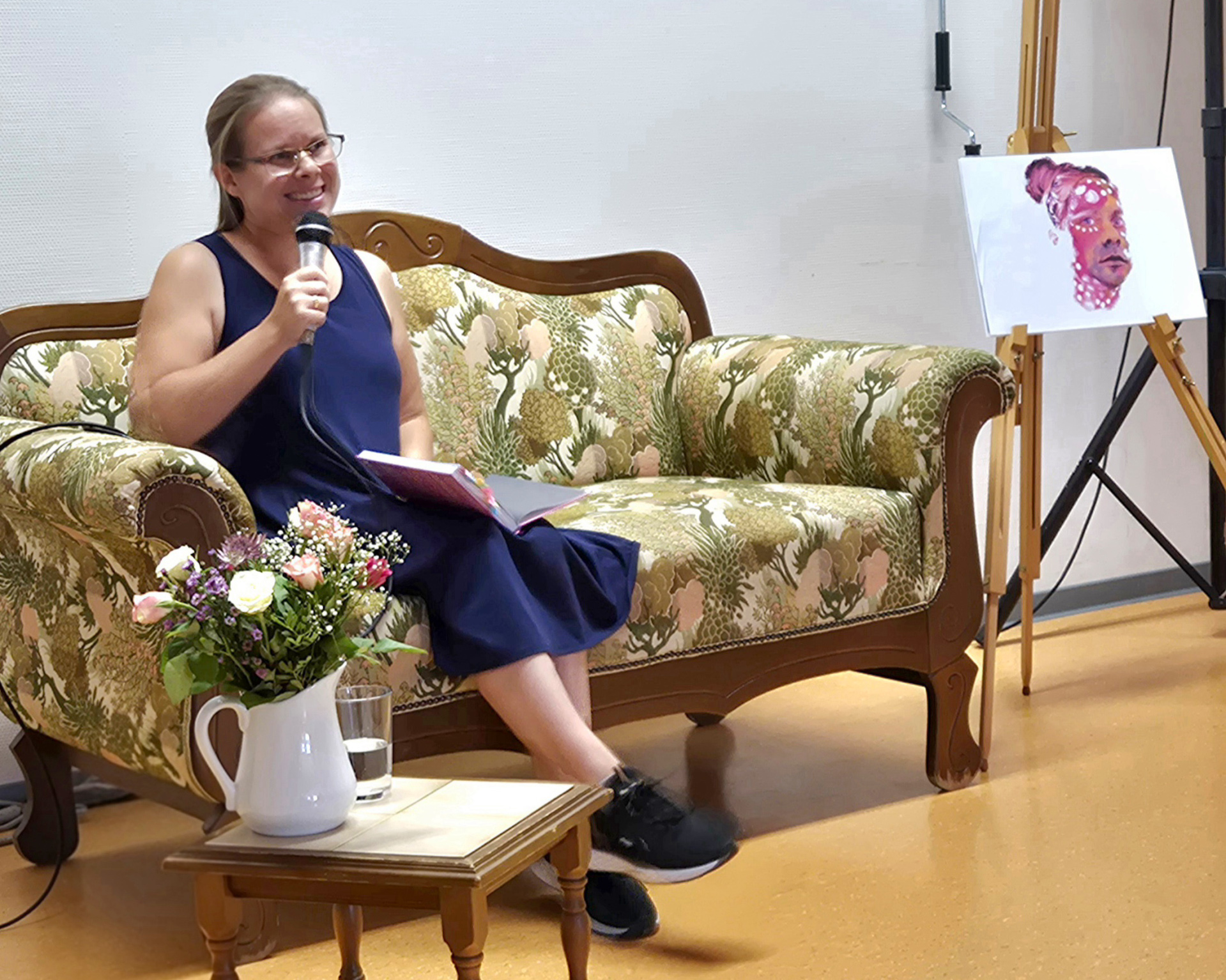 Eine Frau sitzt mit einem Mikrofon in der Hand auf einem Sofa.