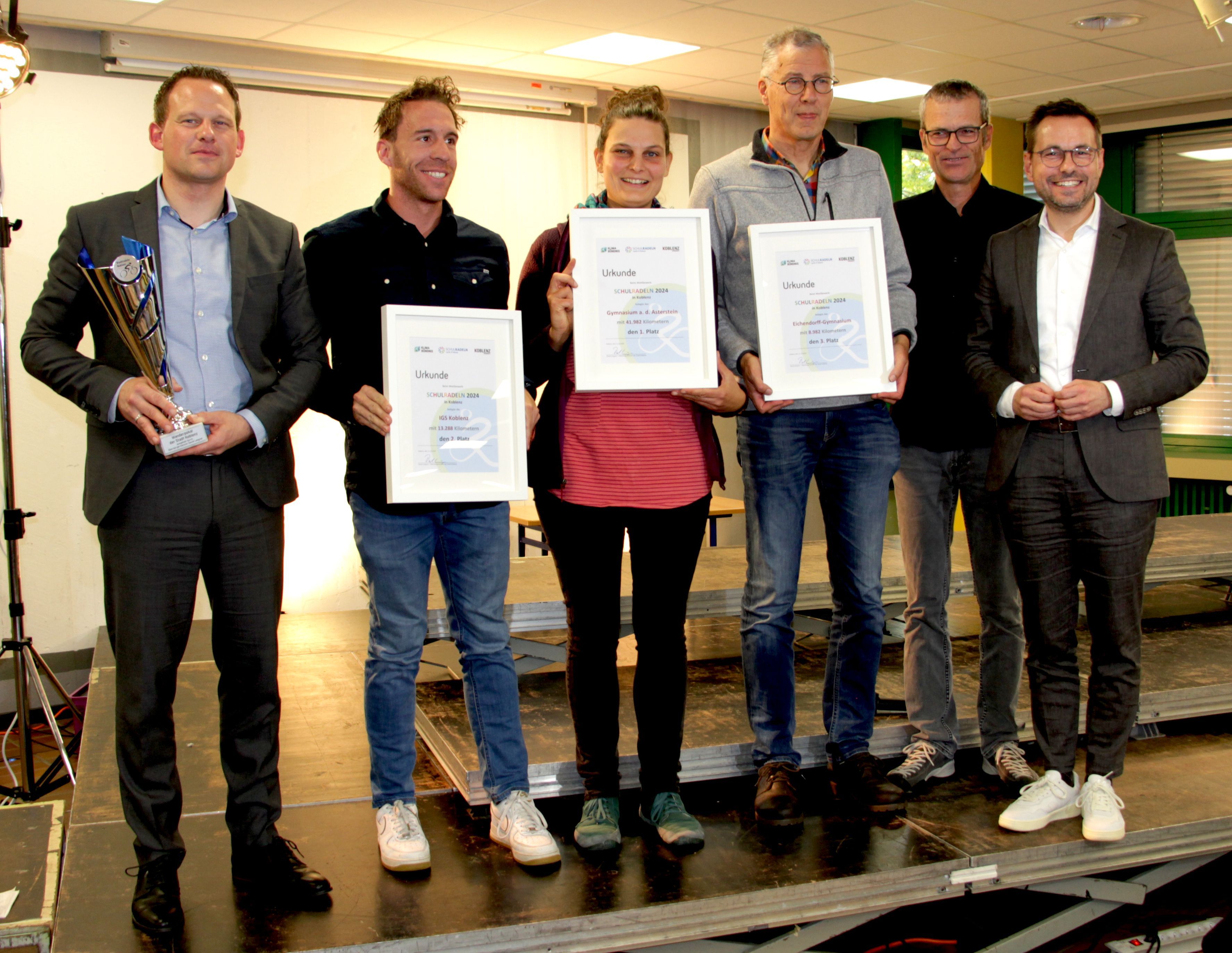 Präsentation des Wanderpokales und der Urkunden nach der Siegerehrung. V. l. n. r. Bastian Staudt, Schulleiter des Gymnasiums auf dem Asterstein; Thomas Nürnberg, Teamcaptain der IGS Koblenz, Anna Grüterich, Teamcaptain des Gymnasiums auf dem Asterstein; Paul Löhnert, Teamcaptain des Eichendorff-Gymnasiums, Ralph Emmerich vom städtischen Radverkehrsteam und der Oberbürgermeister der Stadt Koblenz David Langer.