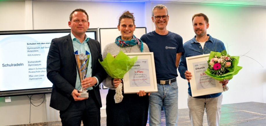 Bei der Ehrung der Schulradeln-Sieger 2026 konnte Ralph Emmerich (2. von rechts) vom Team Radverkehr der Stadt Koblenz Bastian Staudt (von links, Schulleiter des Gymnasiums auf dem Asterstein), Anna Grüterich (Team-Captain Asterstein) sowie Michael Kroll (Team-Captain des Eichendorff-Gymnasiums) für die jeweiligen Schulleistungen ehren. Die Vertreterinnen und Vertreter der IGS Koblenz sind nicht im Bild. Sie mussten ihre Teilnahme an der Veranstaltung kurzfristig absagen. Bei der Ehrung der Schulradeln-Sieger 2026 konnte Ralph Emmerich (2. von rechts) vom Team Radverkehr der Stadt Koblenz Bastian Staudt (von links, Schulleiter des Gymnasiums auf dem Asterstein), Anna Grüterich (Team-Captain Asterstein) sowie Michael Kroll (Team-Captain des Eichendorff-Gymnasiums) für die jeweiligen Schulleistungen ehren. Die Vertreterinnen und Vertreter der IGS Koblenz sind nicht im Bild. Sie mussten ihre Teilnahme an der Veranstaltung kurzfristig absagen.