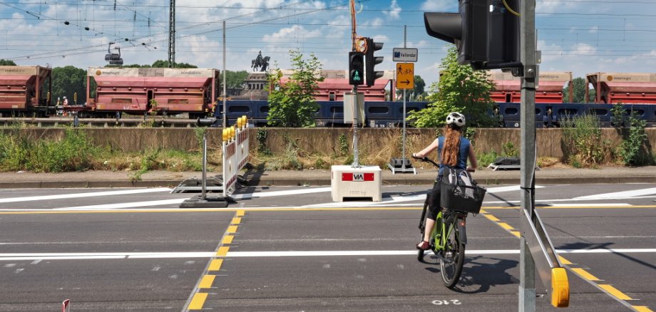 Zur sicheren Überquerung der Bundesstraße von für Radfahrenden und zu Fuß Gehenden wurde eigens eine Ampelanlage mit Anforderungstaster installiert. Auf der gegenüberliegenden Straßenseite ist der baulich getrennte Radweg für Zweirichtungsradverkehr und der Bestandsgehweg zu erkennen. Zur sicheren Überquerung der Bundesstraße von für Radfahrenden und zu Fuß Gehenden wurde eigens eine Ampelanlage mit Anforderungstaster installiert. Auf der gegenüberliegenden Straßenseite ist der baulich getrennte Radweg für Zweirichtungsradverkehr und der Bestandsgehweg zu erkennen.
